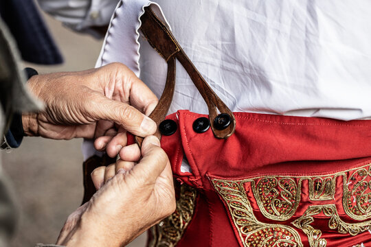 Closeup of unrecognizable male fastening buttons on traditional red costume of matador preparing for corrida event