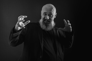 Smiling business man with beard showing man, gesturing with hands, showing something, isolated on dark background. Low key. The portrait is emotional