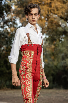 From below young matador wearing red traditional costume standing in nature while looking at camera