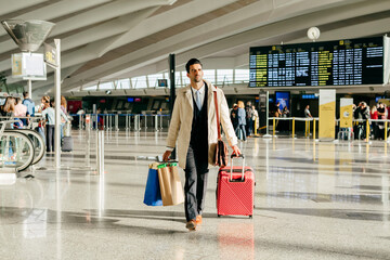 Man with dark hair in stylish clothes walking with suitcase in terminal of airport