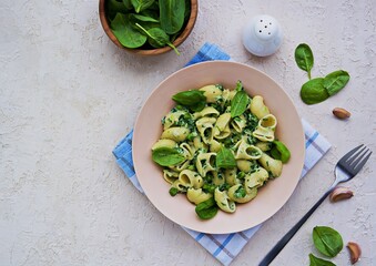 Spring green pasta with spinach and green peas in a creamy sauce in a beige clay plate on a light concrete background.