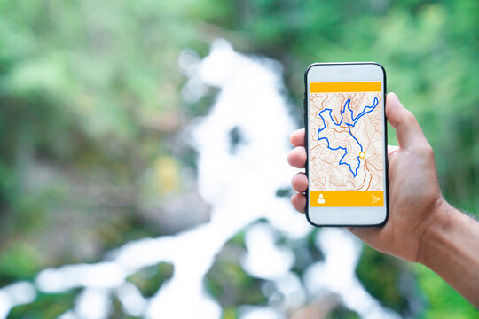 Cropped unrecognizable man traveler using smartphone browsing on map app standing on slope of amazing landscape of green forest with fast river