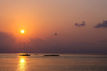 Sunset over ocean and a boat in Maldives.