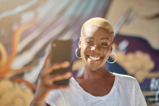 Smiling African American female with short hair taking self portrait on smartphone camera in cafe