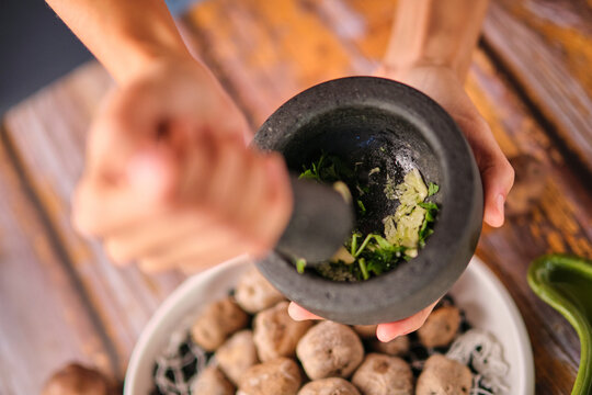 From above of crop unrecognizable chef crushing spices in pounder with pestle above cooked potatoes