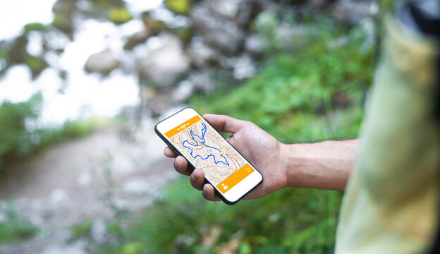 Cropped unrecognizable man traveler using smartphone browsing on map app standing on slope of amazing landscape of green forest with fast river