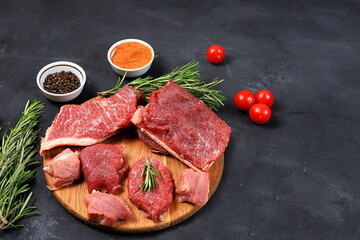 Fototapeta na wymiar Fresh beef steak with ingredients for cooking on an old table, raw meat with rosemary, pepper, tomatoes, for grilling or skillet, cooking, top view, place for text