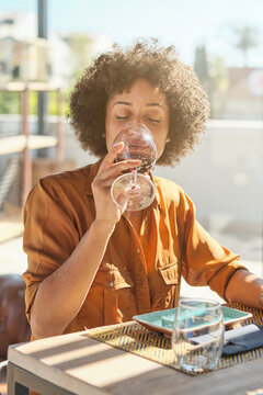 African American female sitting at table in cafe drinking wine in glass