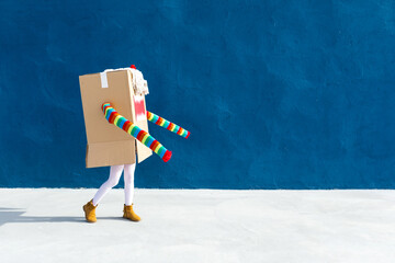 Unrecognizable playful kid wearing funny costume of monster made of carton box standing on street during holiday celebration
