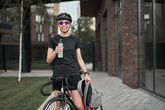 Female cyclist courier with bottle in his hands on street on summer day