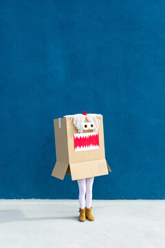 Unrecognizable playful kid wearing funny costume of monster made of carton box standing on street during holiday celebration