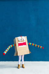 Unrecognizable playful kid wearing funny costume of monster made of carton box standing on street during holiday celebration