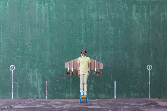 Cheerful male in handmade cardboard wings standing looking up while dreaming about achieving success