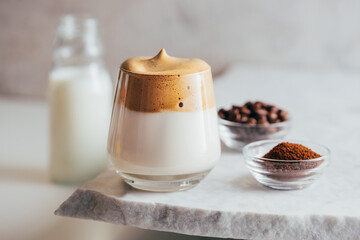 Aromatic Dalgona beverage in glass placed on edge of marble table with instant coffee and beans