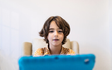 Concentrated child with netbook at table sitting on couch at home