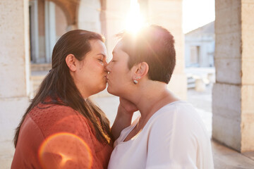 Side view of homosexual couple of women kissing with closed eyes near old house in sunlight in back lit