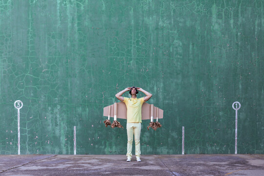 Male in handmade cardboard wings standing looking up while dreaming about achieving success