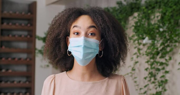 Portrait Of Afro American Girl In Medical Protective Surgical Mask Nurse Student Ethnic Black Woman With Curly Hair Waves Her Hand In Greeting Wishes Gesture Hello To Camera Looks And Talks Remotely