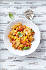 Pasta with chicken breast, cherry tomatoes and fresh basil. Bright wooden background. Top view.	