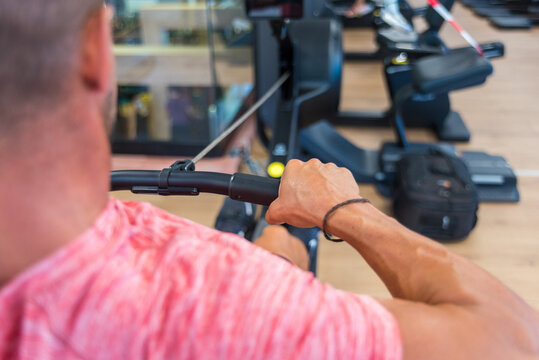 Back view athletic male doing exercises on rowing machine while training in modern gym