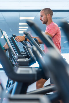 Side view of handsome male doing exercises on elliptical machine during cardio workout in modern sports club