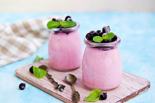 Dessert, airy mousse whipped cream and mashed black currants in portion jars on light blue background.