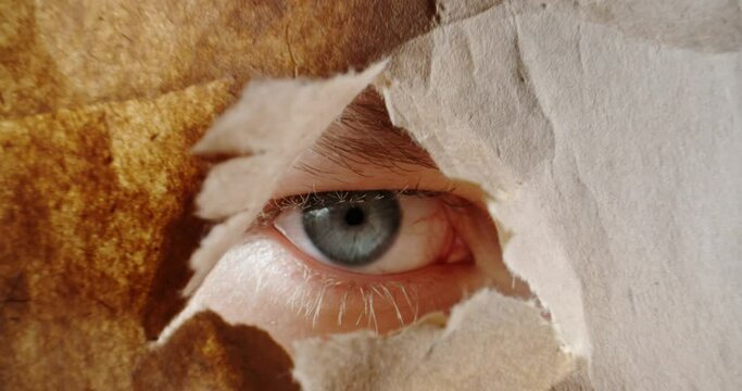 Male Eye looking and peeping through cardboard hole - mistery, secret, subconsciousness, big brother, enigma concept 4k footage zoom extreme close up