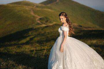 Fototapeta na wymiar Beautiful young bride stand on the hill in mountais. Windy outdoor. Green hills on background