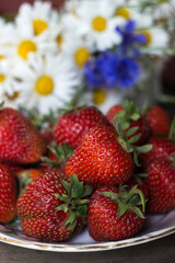 Summer flowers chamomile and cornflowers and strawberries in a plate. Flowers and fruits, background