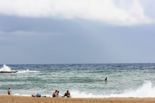 A group of people are relaxing on the Mediterranean coast on a cloudy summer day, the sea is stormy and the clouds are thickening before it rains.