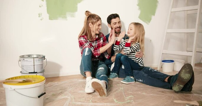 Joyful family spending time together. Caucasian mother and father talking and playing with small adorble preschool girl daughter resting sitting on floor after home renovation and improvement.