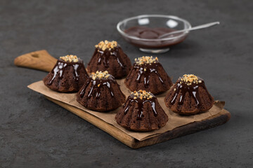 Dessert chocolate muffins with icing and nut sprinkles on paper on a dark background