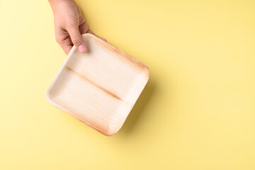 Hand holding betal palm leaf plate (Biodegradable, Compostable, Disposable or Eco friendly plate) on yellow background, Sustainable concept