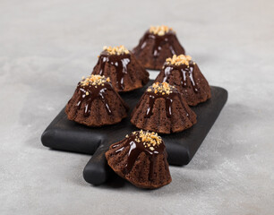 Cacao mini muffins with chocolate icing and nut sprinkles on wooden board on a light gray background