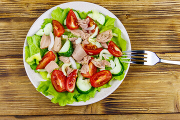 Tasty tuna salad with lettuce and fresh vegetables on wooden table. Top view