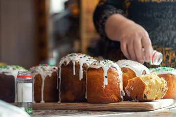 Senior woman cooking Traditional eastern europe Russian and ukrainian Easter cake kulich decorated with sweet sugar icing on wooden table morning sunlight ray. Tasty handmade orthodox paska bread