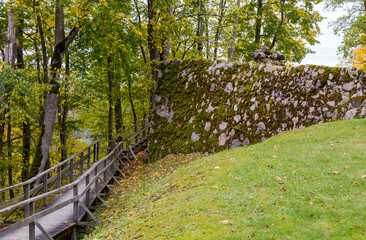 Wooden forest path and the fragment of stone wall of the Sigulda Medieval Castle, Latvia. It was built by the Livonian Brothers of the Sword who were later incorporated into the Teutonic Order.
