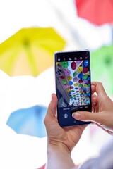 Vertical photo. Hand with smartphone in hand takes off colorful umbrellas over pedestrian street