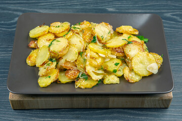 cooked fried potatoes with herbs and vegetables in a plate on a wooden table