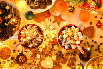 sweet food top view background for merry christmas or new year holiday decoration with night illumination - chocolate candies, tangerines, cookies, marshmallow and cocoa latte on white wood
