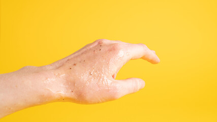 Left hand with scrub peeling gel that has black dots on yellow background