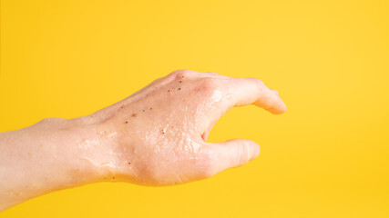 Fototapeta premium Left hand with scrub peeling gel that has black dots on yellow background