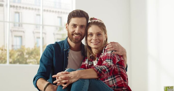Caucasian joyful young couple wife and husband sitting in room hugging together, embracing, looking at camera and smiling. Family time. Repair and improvement. renovate home. Close up concept