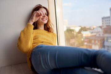 a pretty woman in a yellow sweater lies on the windowsill and looks out the window