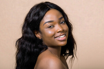 Portrait of smiling pretty young african american woman with natural makeup and long dark hair, looking at camera isolated on beige background. Beauty, skin care, people, races concept
