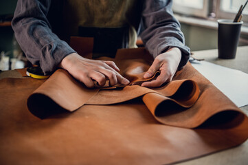 A young apprentice in a boot workshop prepares leather for further use on a large table.