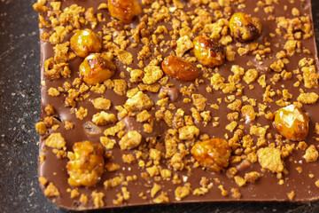 Milk chocolate bar with whole and cracked nuts and caramel on a black background. Top view