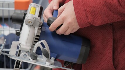 Woman in a shop chooses a portable, electric circular saw. Concept of women's independence, repair, construction and design. Screen from video footage