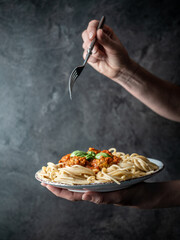 Female hand holding plate of spaghetti with roasted meatballs in tomato sauce on vintage table. Traditional italian cuisine. Dark and moody.