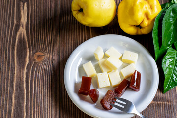 Slices of quince marmalade and cheese on the white plate for dessert. Fresh ripe quince fruit on the wooden home table. Healthy eating concept.